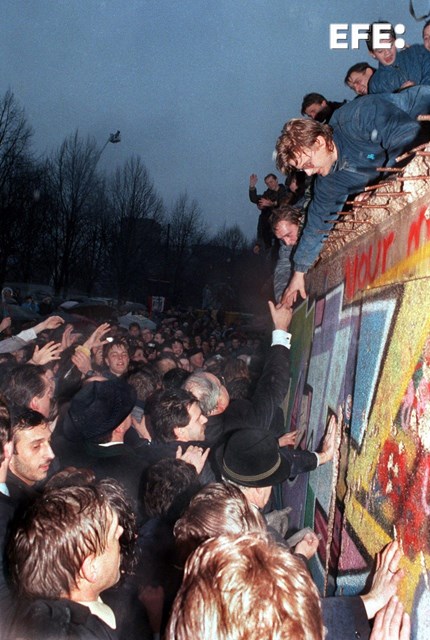 Berlín (Alemania), 22/12/1989.- El canciller alemán, Helmut Kohl (c), estrecha la mano a un ciudadano berlinés que se encuentra encaramado en lo alto del Muro de Berlín cerca de la Puerta de Brandemburgo en Berlín. EFE